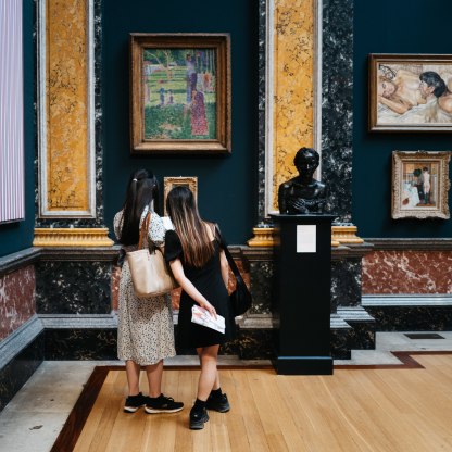A highlight image for two visitors look at a painting in a gallery at the museum